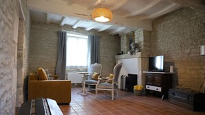 A room with a stone wall, a wooden bench, a sofa, a chair, a small table, a television, and a fireplace.