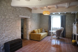 Um quarto com parede de pedra, sofá, poltrona, mesa pequena e luminária pendente.