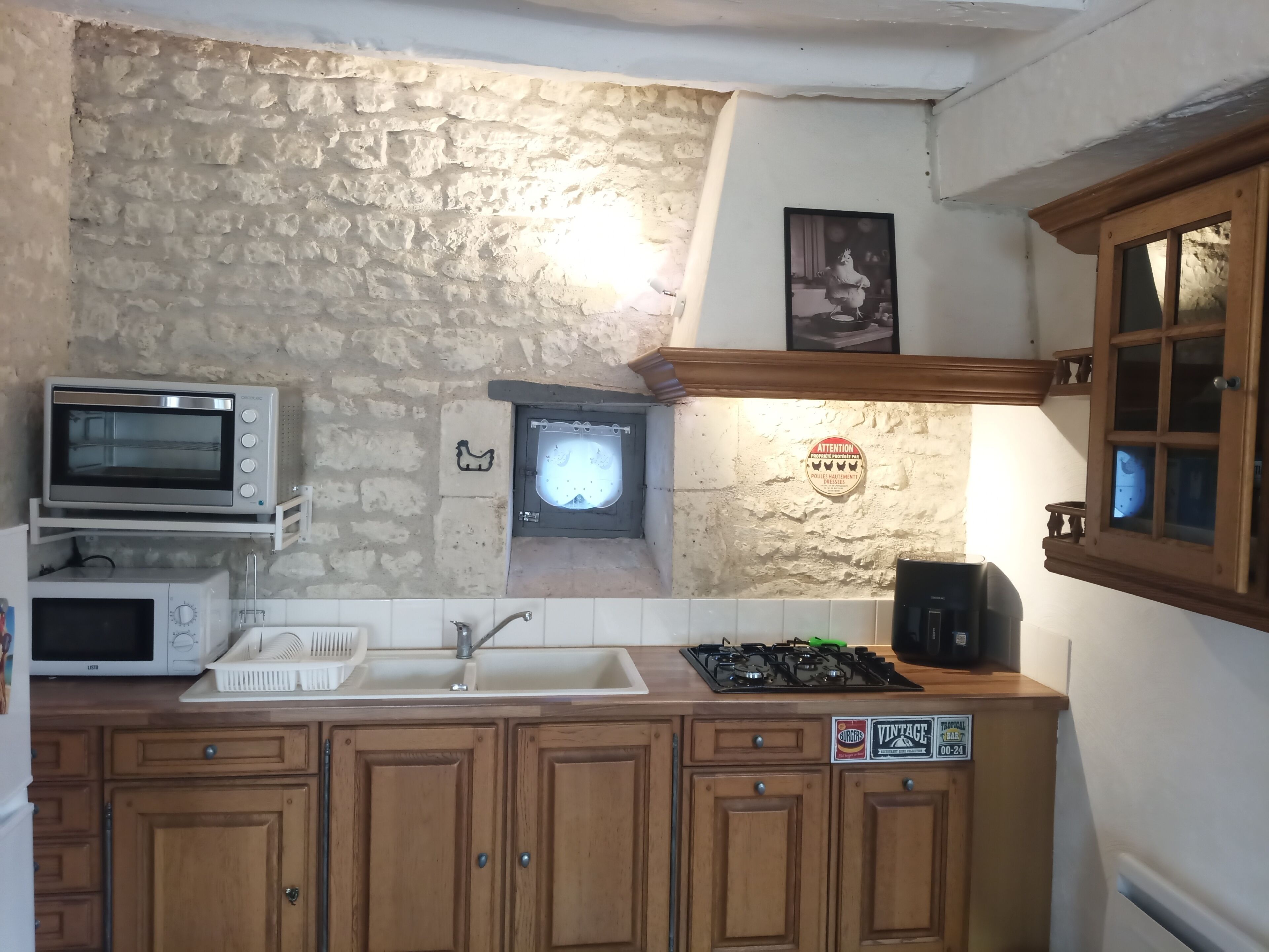 A kitchen with a stone wall, a sink, a stove, and wooden cabinets.