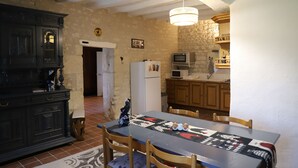 A dining area with a table, chairs, a chandelier, a refrigerator, and a microwave in the background.