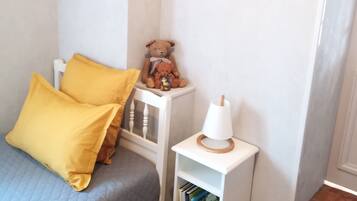 A bedroom with a bed, a small bedside table with a lamp, a bookshelf, and a teddy bear.