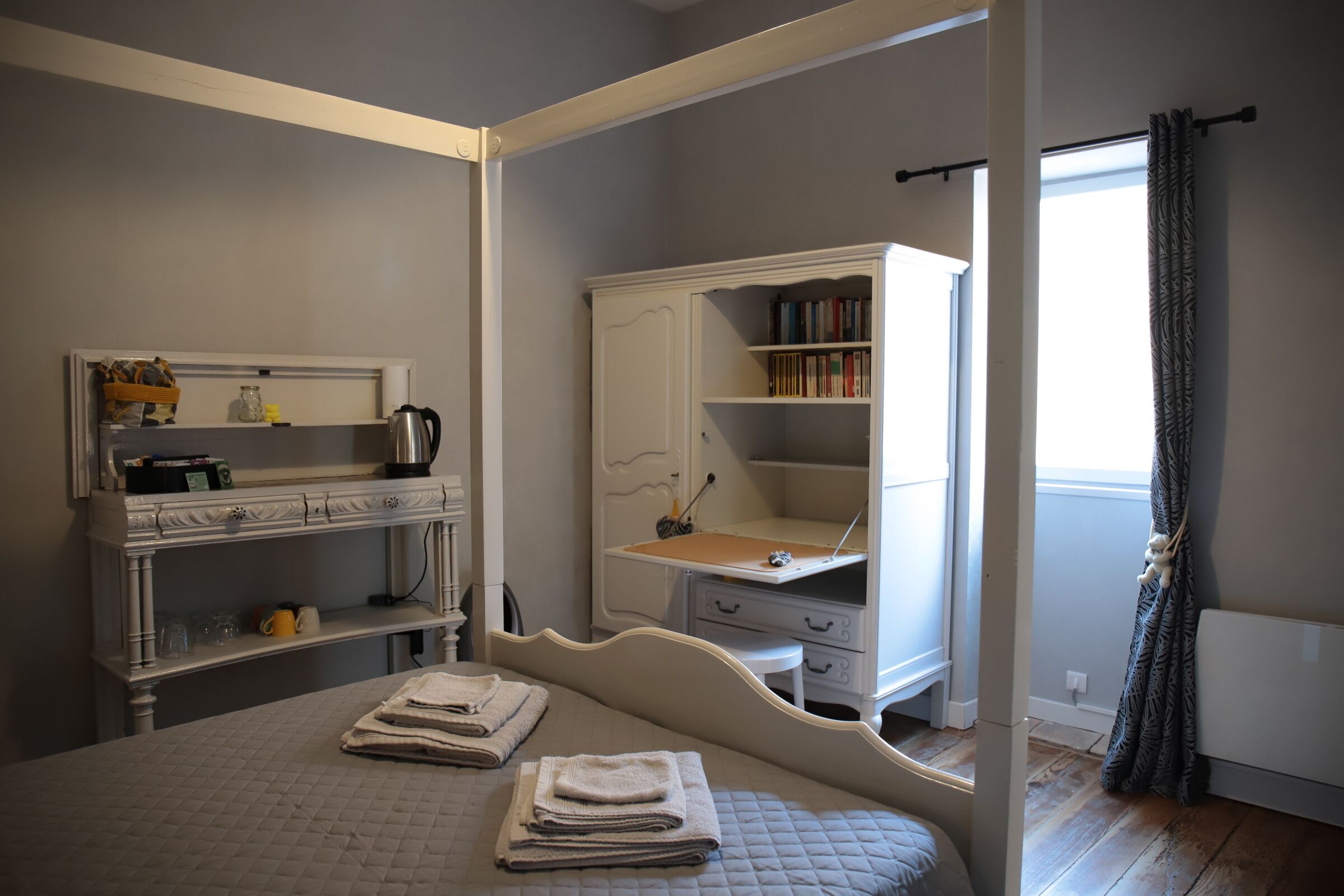 Een slaapkamer met een bed, een bureau, een boekenkast en een raam met gordijnen.