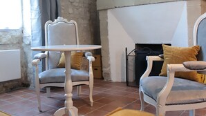 A room with stone walls, a fireplace, a mirror, and two chairs with cushions.