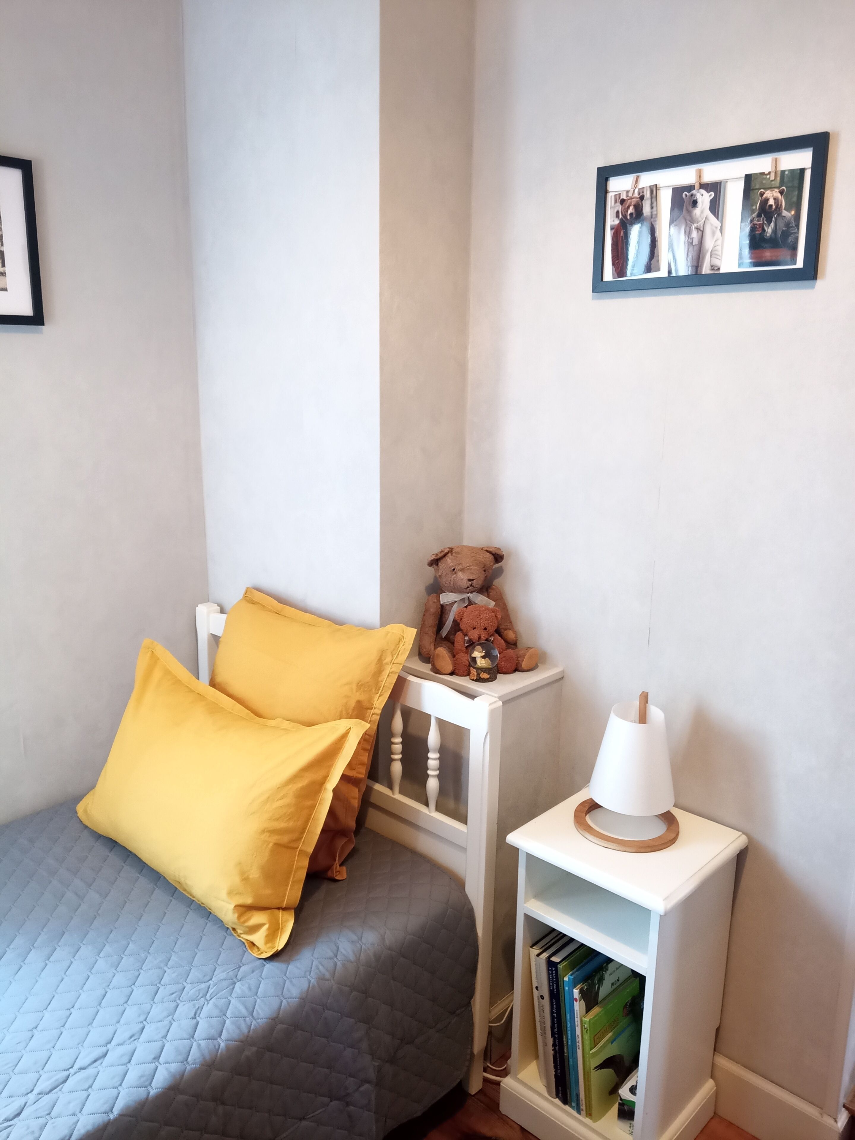 Une chambre à coucher avec un lit, une table de chevet avec une lampe, une bibliothèque et un ours en peluche.