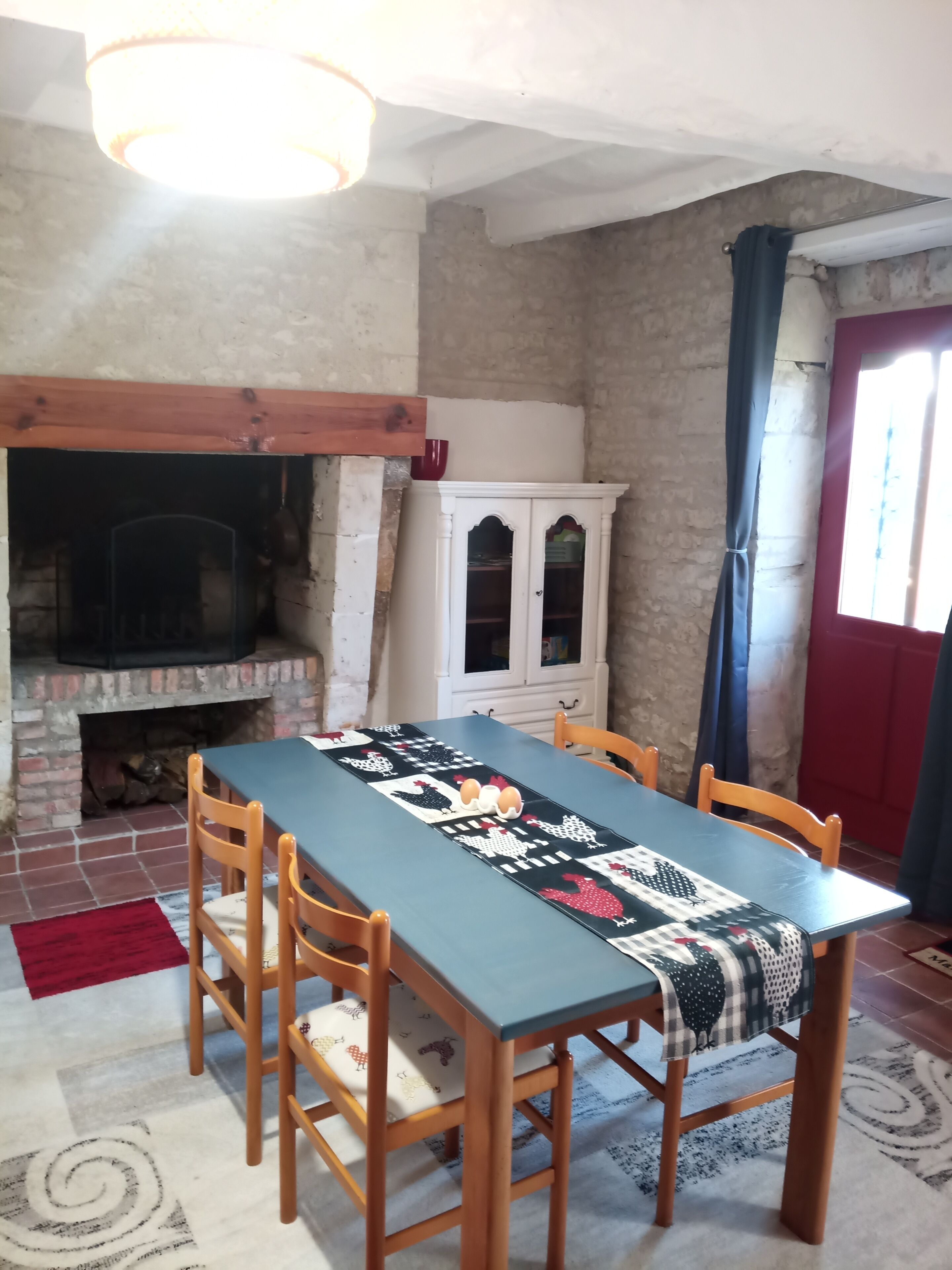 Un'area pranzo con tavolo apparecchiato per quattro persone, camino, un armadietto e una porta rossa.