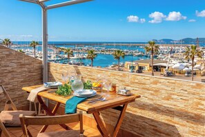 A balcony with a table set for dining, overlooking a marina with boats and palm trees. - ClickSardegna Grand Sunset Penthouse with 2 Seafront Terraces & Private Garage (Alghero)