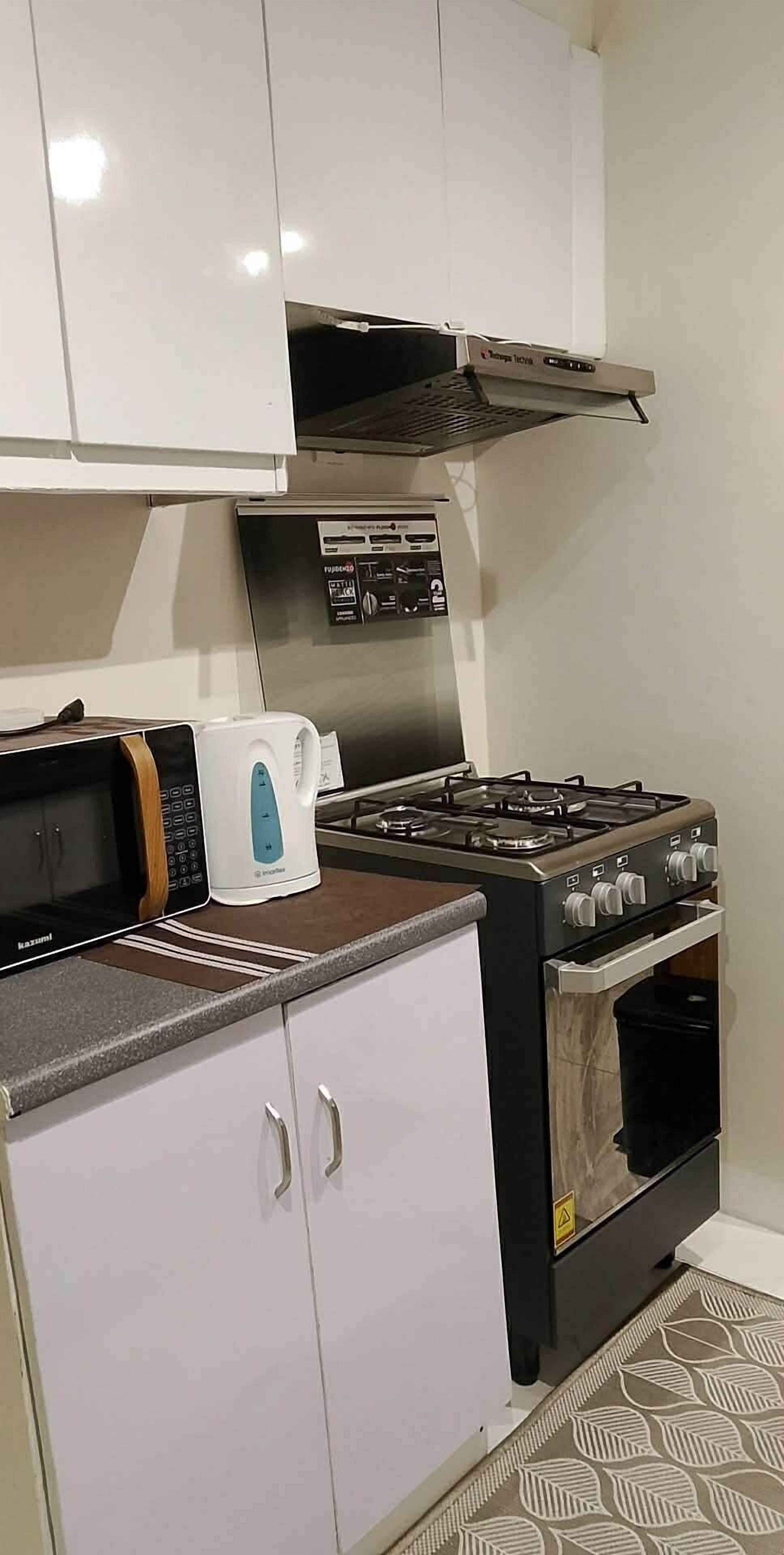 Cocina compacta con microondas, hervidor, estufa, horno y armarios blancos.