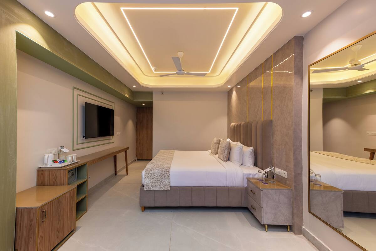 Un dormitorio moderno con cama, mesita de noche, espejo, televisor y estanterías empotradas.
