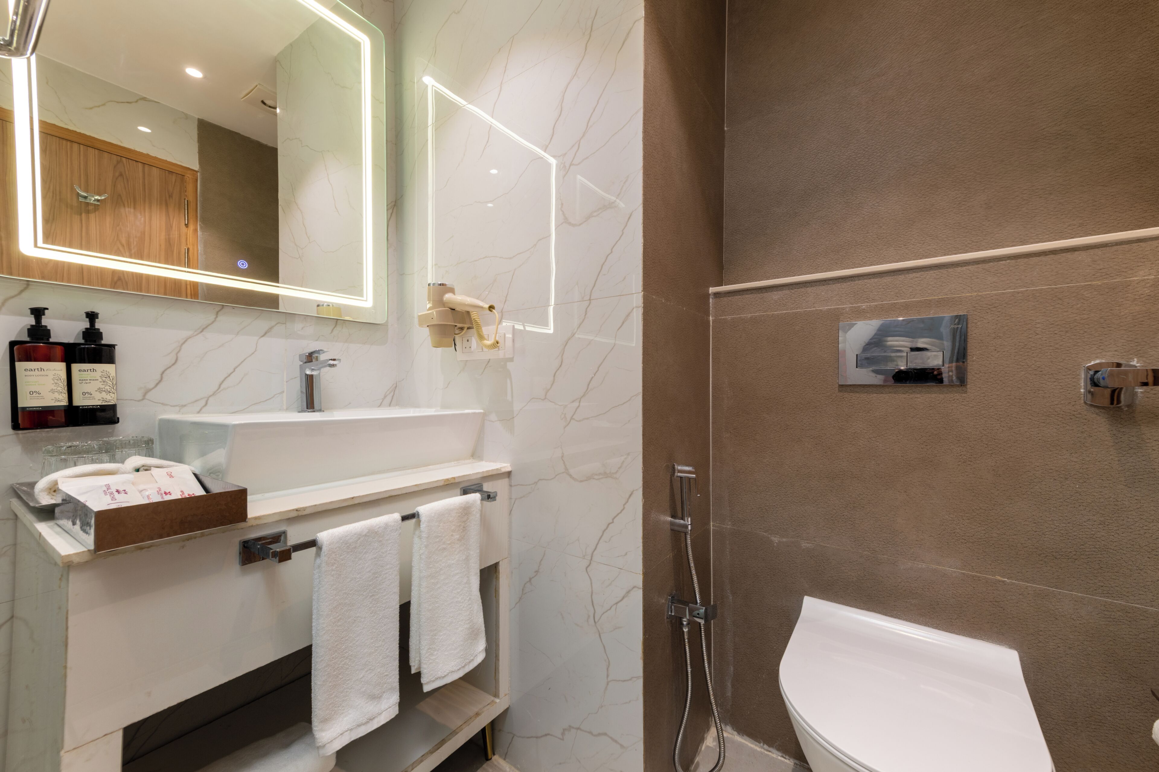 Un baño moderno con tocador de mármol, un espejo grande con iluminación LED, cabina de ducha y un inodoro.