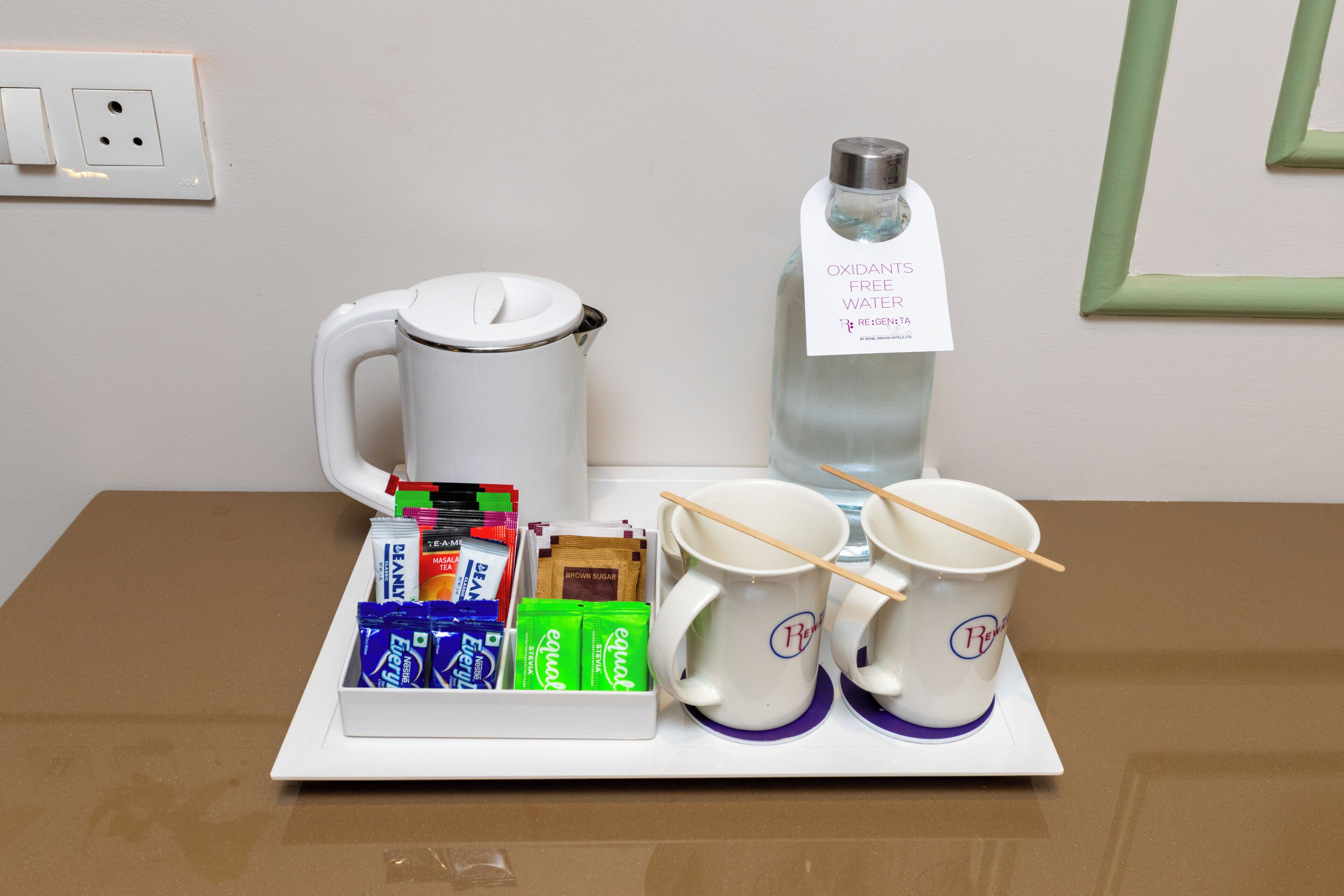 A tray with a white coffee maker, a water bottle, two white mugs with wooden spoons, and a box of tea bags.