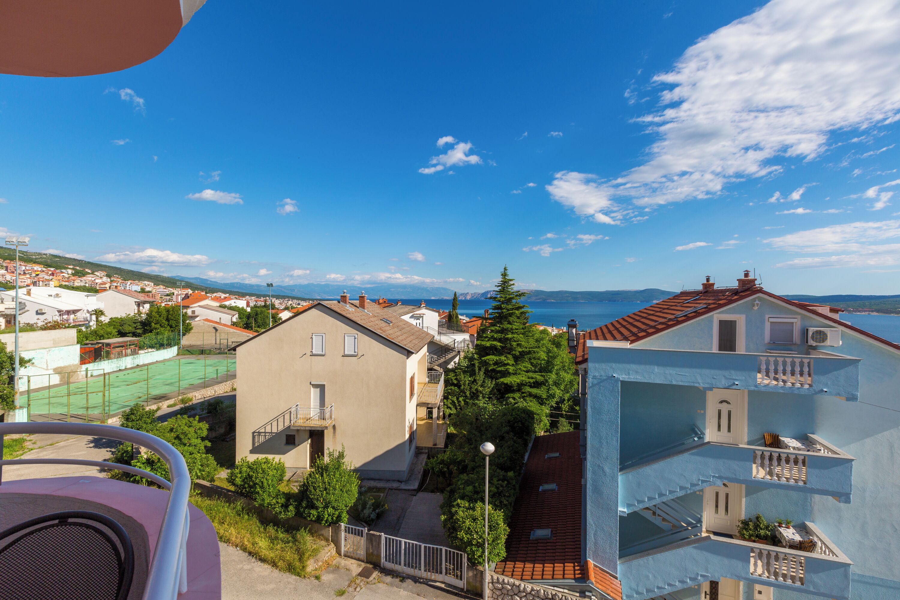 A residential area with multi-story buildings, a tennis court, and a clear view of the sea.