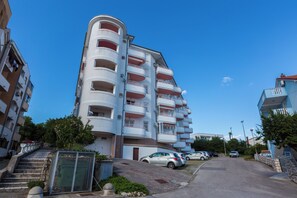 Ein mehrstöckiges Wohngebäude mit Balkonen, einem Parkplatz und blauem Himmel.