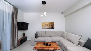 A modern living room with a sectional sofa, a wooden coffee table, a flat-screen TV, and a painting on the wall. - Etherio Naxos Anemos Tranquil 2-bedroom apartment with AC in beautiful Naxos (Naxos)