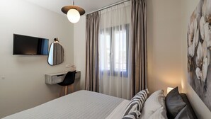 A hotel room with a bed, a desk with a chair, a TV, and a painting on the wall. - Etherio Naxos Anemos Tranquil 2-bedroom apartment with AC in beautiful Naxos (Naxos)