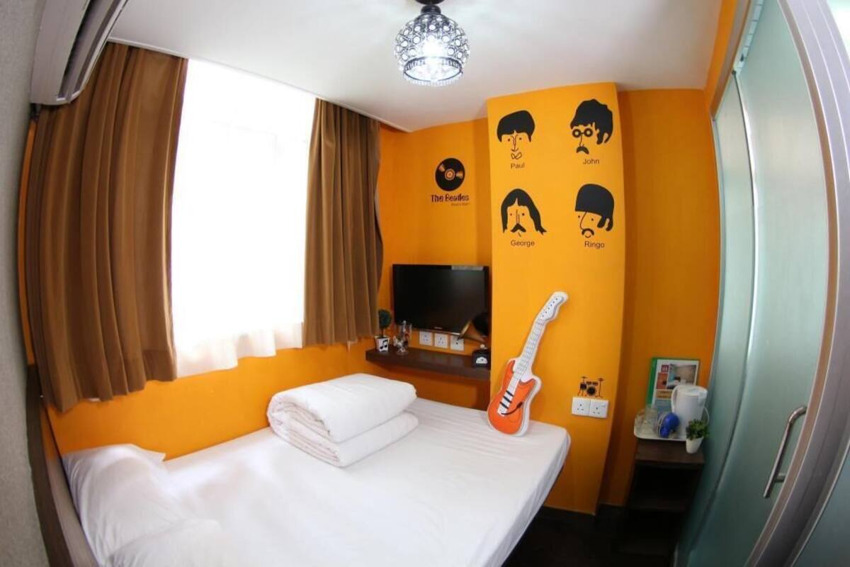 A hotel room with a bed, a guitar, a television, and wall art featuring band members.