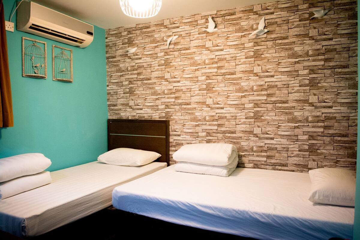 A room with two single beds, a teal wall, a stone-patterned wall, and an air conditioning unit.