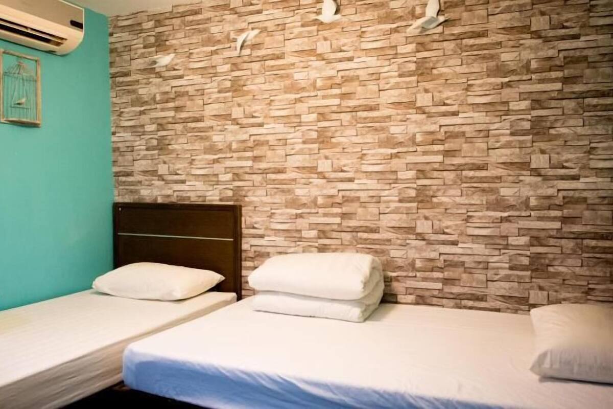 A room with two single beds, a stone wall, and an air conditioning unit.