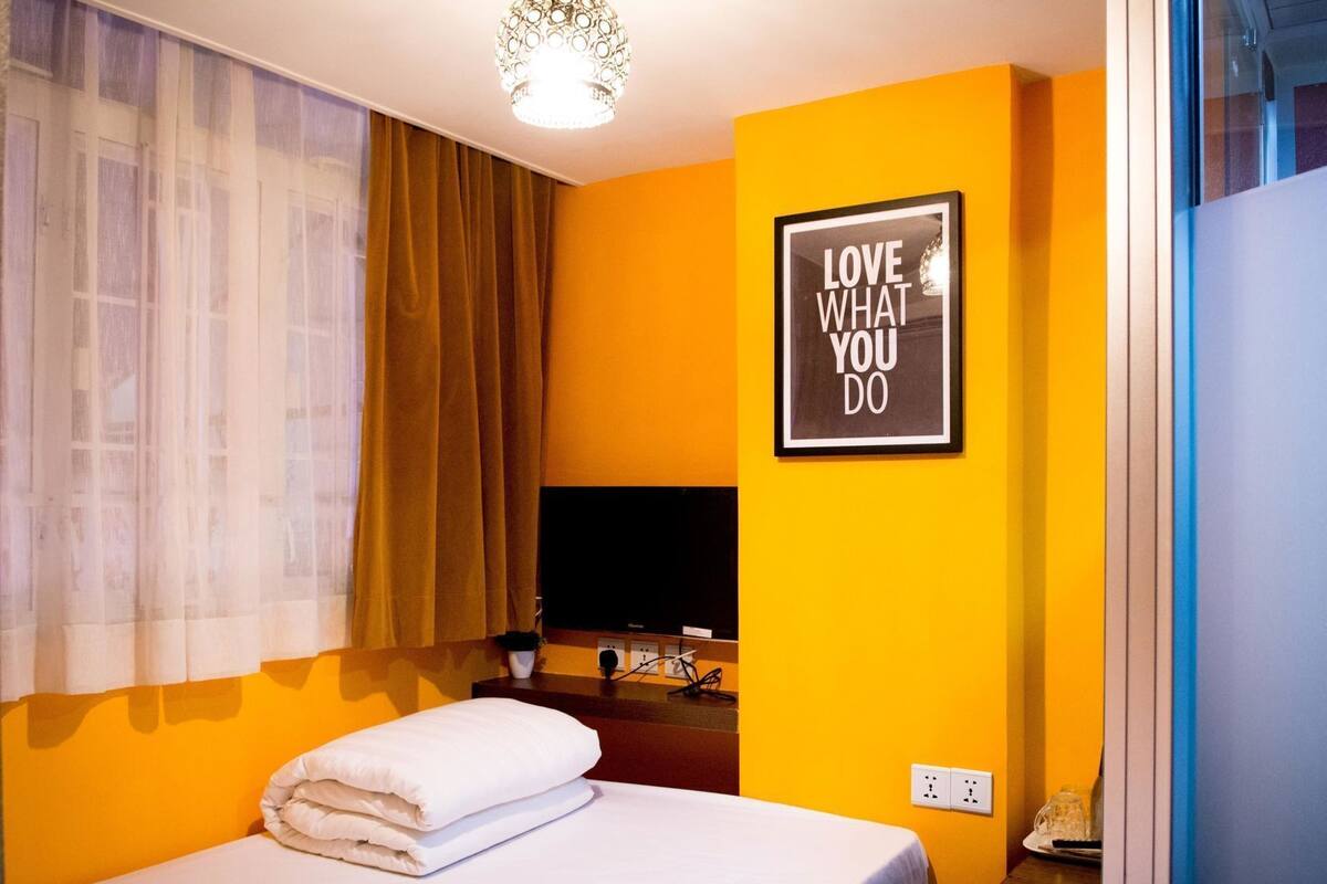 A hotel room with a bed, a TV, a framed motivational quote on the wall, and a window with curtains.