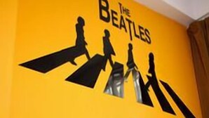A wall with a Beatles-themed decoration, a television, and a small shelf with decorative items. - Tempo Inn @david Mansion (Kowloon)