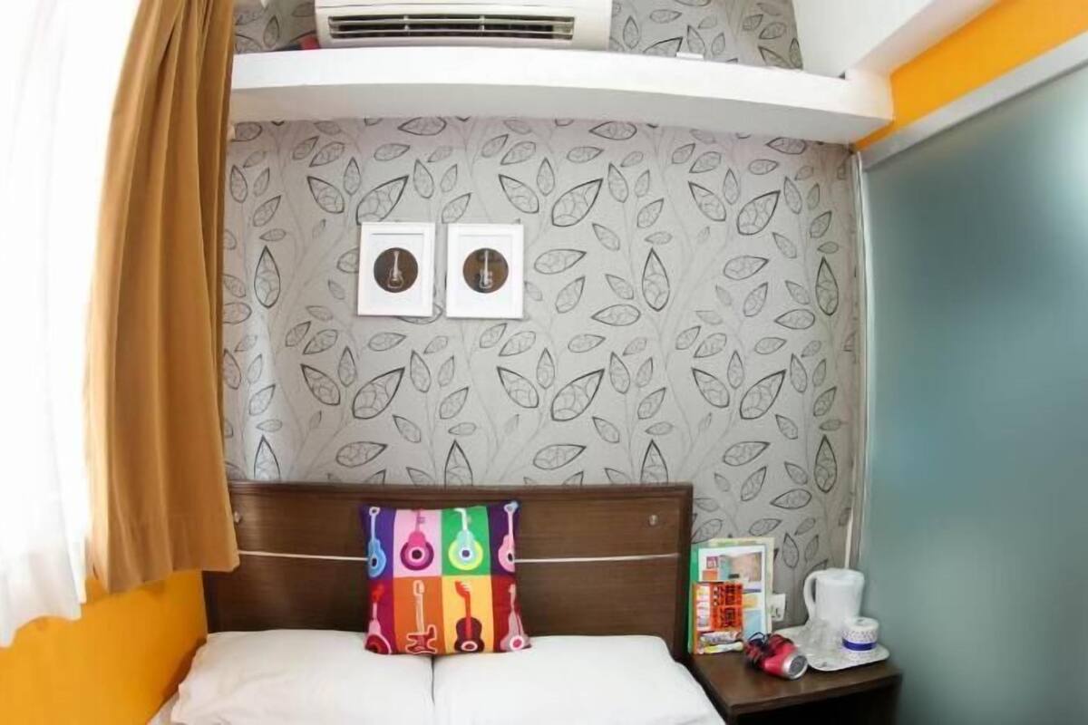 A hotel room with a bed, a nightstand, a small table, a wall-mounted air conditioner, and a curtain.