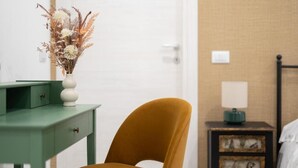 Een kamer met een groen bureau, een gele stoel, een nachtkastje met een lamp en een deur.