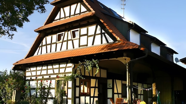 A traditional half-timbered house with a sloped roof, a visible chimney, and a front porch with a table and chairs. - Apartment 'Rheinaue' with Shared Garden, Balcony and Wi-Fi (Neuried)