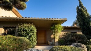 Een modern huis met pannendak, een houten deur en een verzorgde tuin met rotsen en struiken.