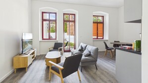 Un salon moderne comprenant un canapé, des fauteuils, un téléviseur et un coin repas avec une table et des chaises.