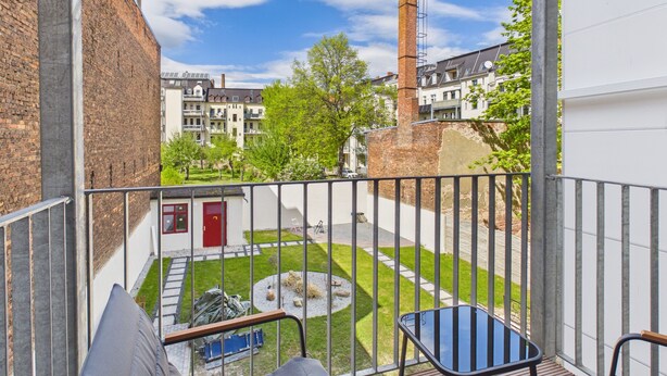 Un balcon donnant sur une cour, une porte rouge et une cheminée en briques.