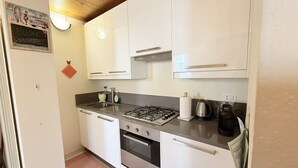 Eine kleine Küche mit weißen Schränken, einem Gasherd, einem Wasserkocher und einer Kaffeemaschine.