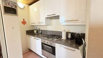 Una cocina compacta con armarios blancos, estufa a gas, hervidor y cafetera.