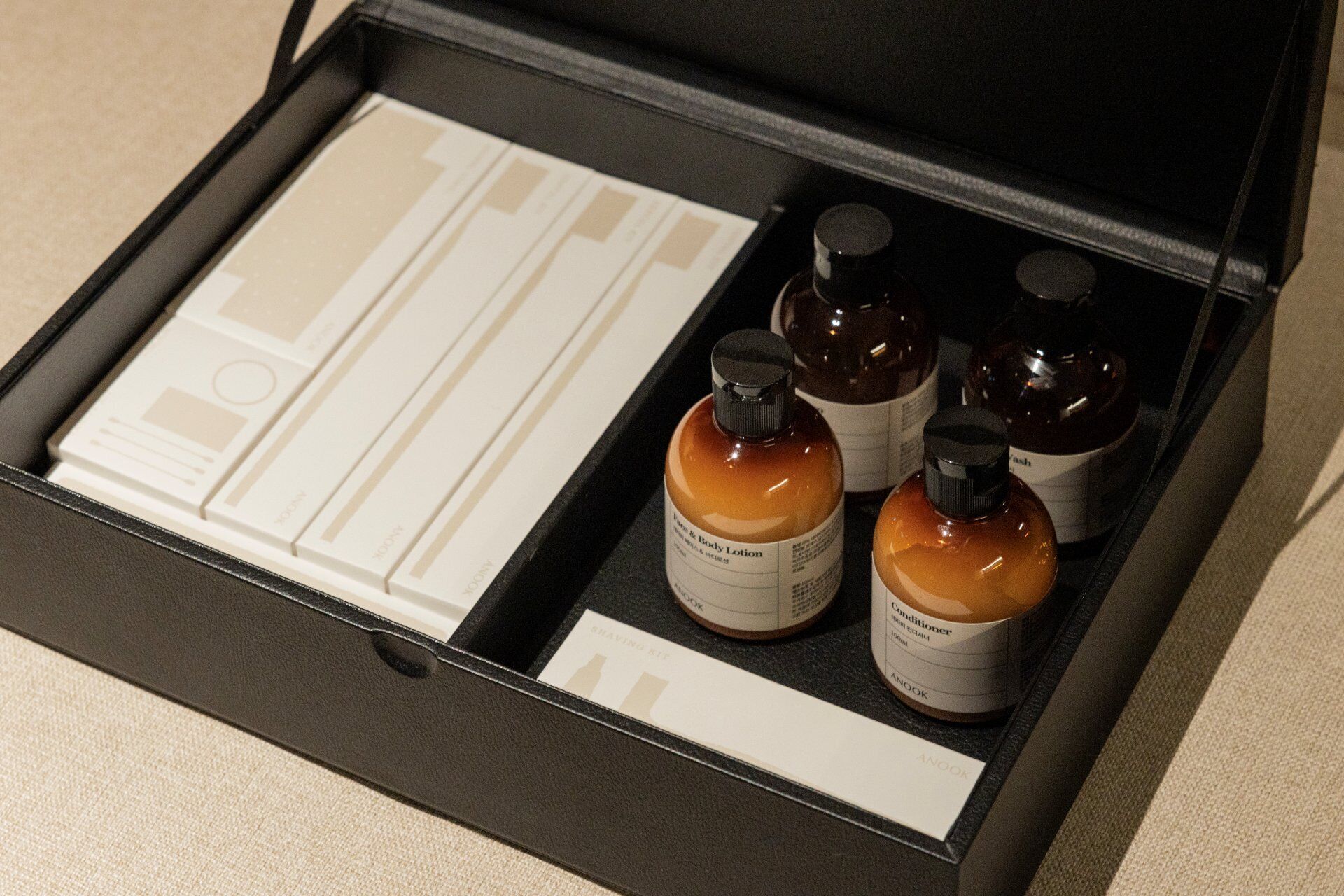 A black box containing a toiletry kit with a face and body lotion, conditioner, and a travel-sized toiletry set.