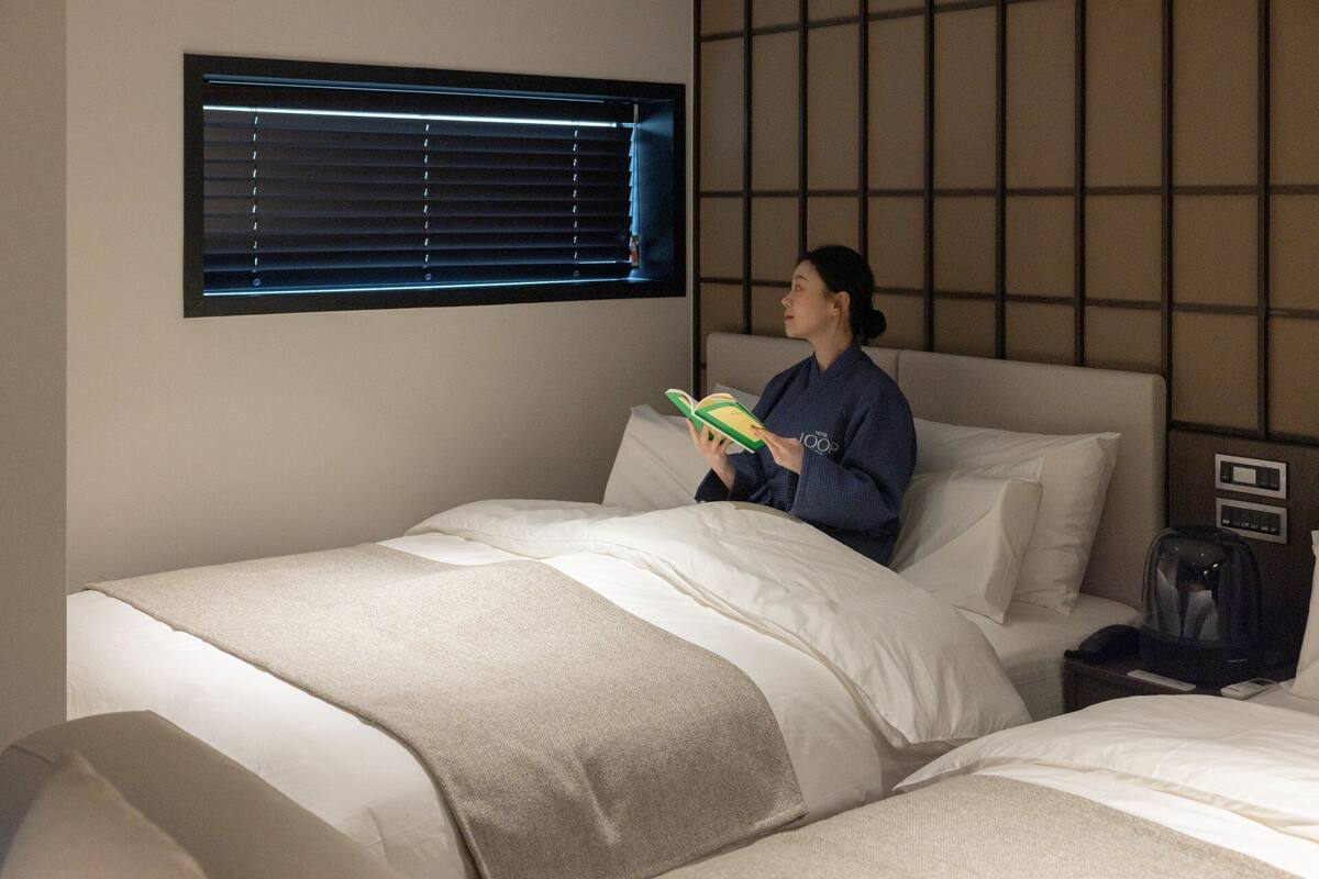 Ein Hotelzimmer mit Bett, Fenster mit Jalousien, Nachttisch und Beistelltisch.