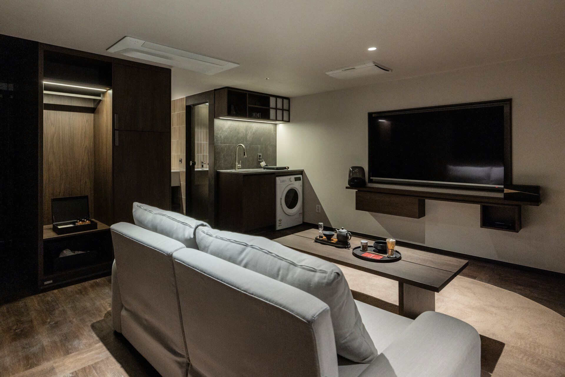Una sala de estar moderna con sofá, mesa de centro, televisor, lavadora y cocina integrada.