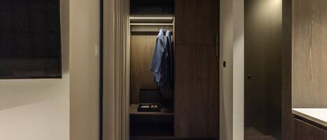 A narrow hallway with a wooden floor, a closet with hanging clothes, and a door on the right.