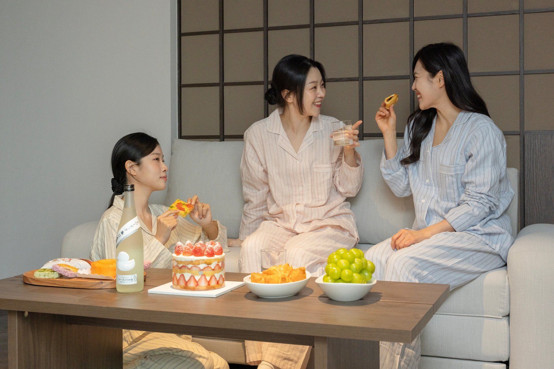Three people sitting on a couch, eating and drinking.