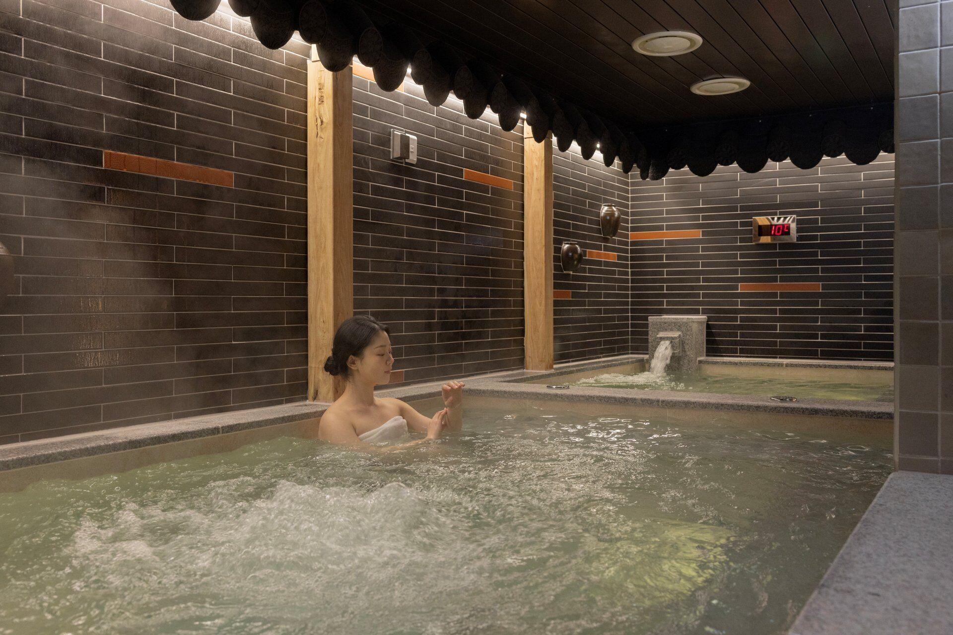 A person in a hot tub with a digital thermometer indicating 10°C.
