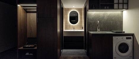 Un baño moderno y compacto con lavadora integrada, un lavabo con espejo y una pequeña zona de estar.