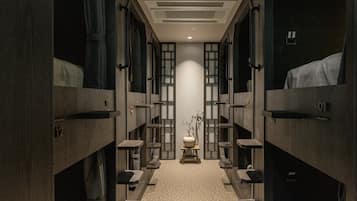 A narrow hallway with bunk beds on either side, a central light fixture, and a small table with a vase.