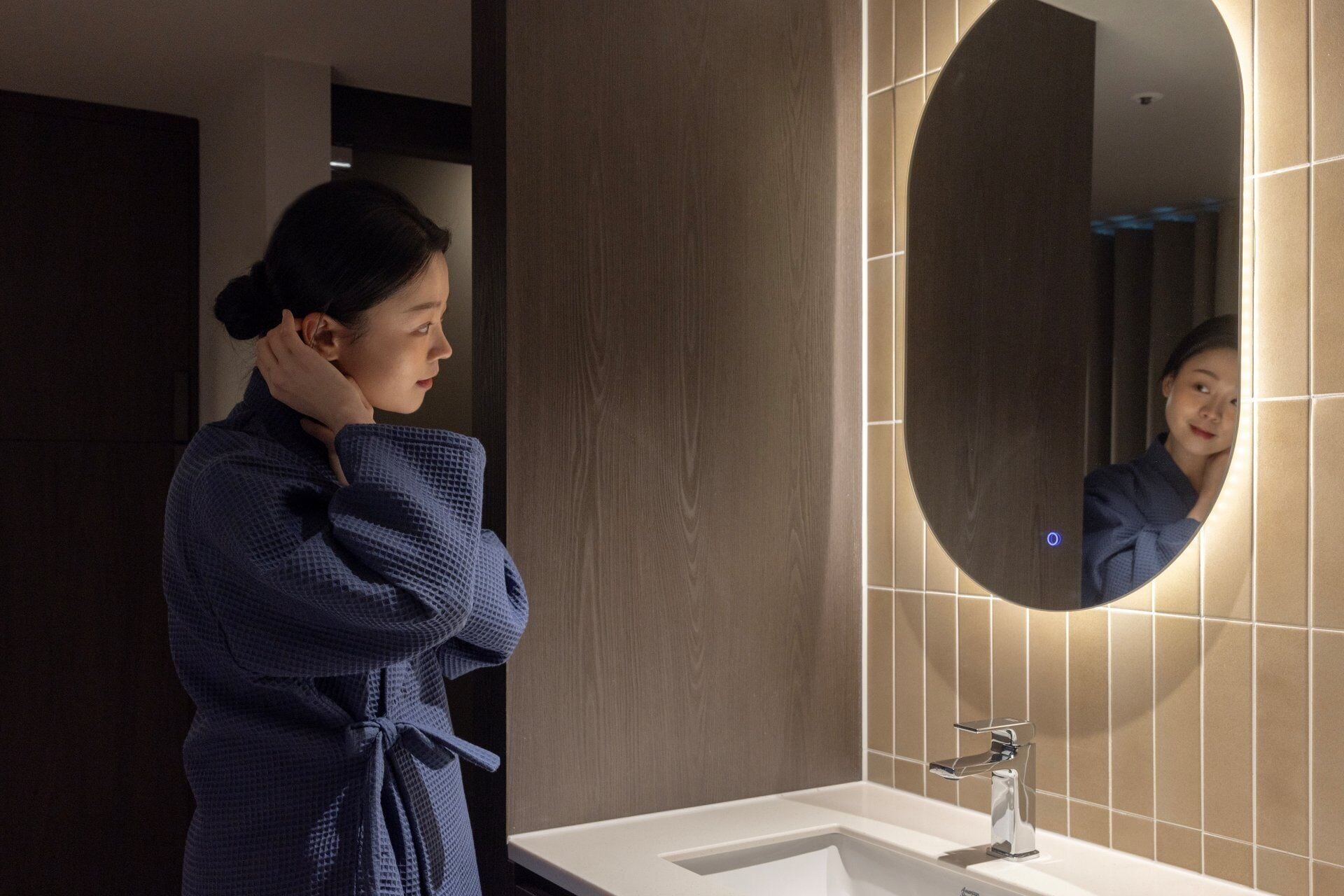 A person in a robe standing in front of a bathroom sink with a mirror.