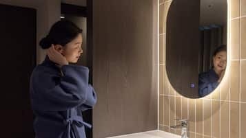 A person in a robe standing in front of a bathroom sink with a mirror.