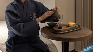 A person in a robe pouring tea into a cup, with a small table featuring a bowl and a decorative item. - LOOP Seoul Hotel Retreat by Anook Seoul Gangnam 1 (Seoul)
