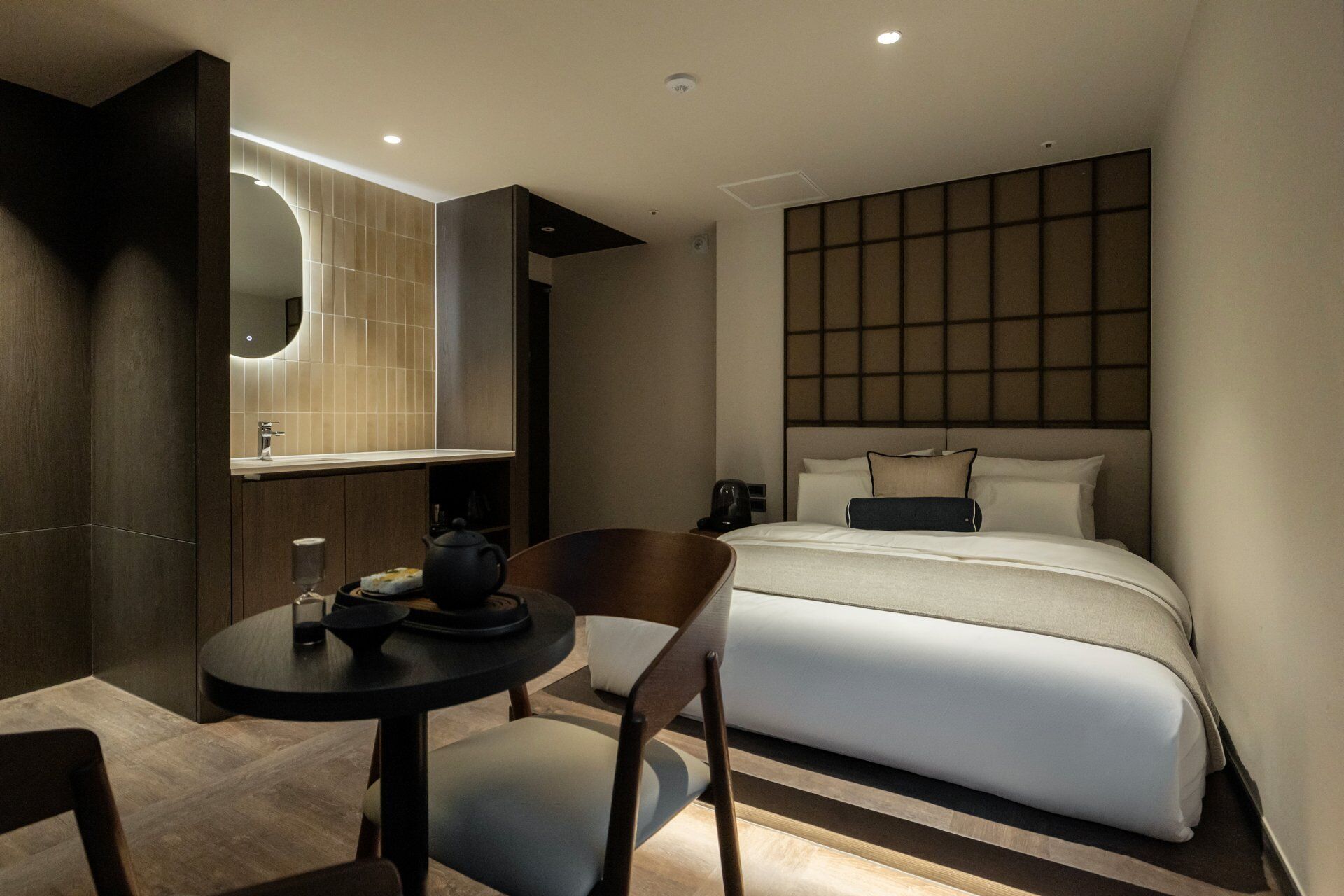 Une chambre d’hôtel moderne équipée d’un lit, d’une table de chevet, d’une chaise et d’un grand miroir.