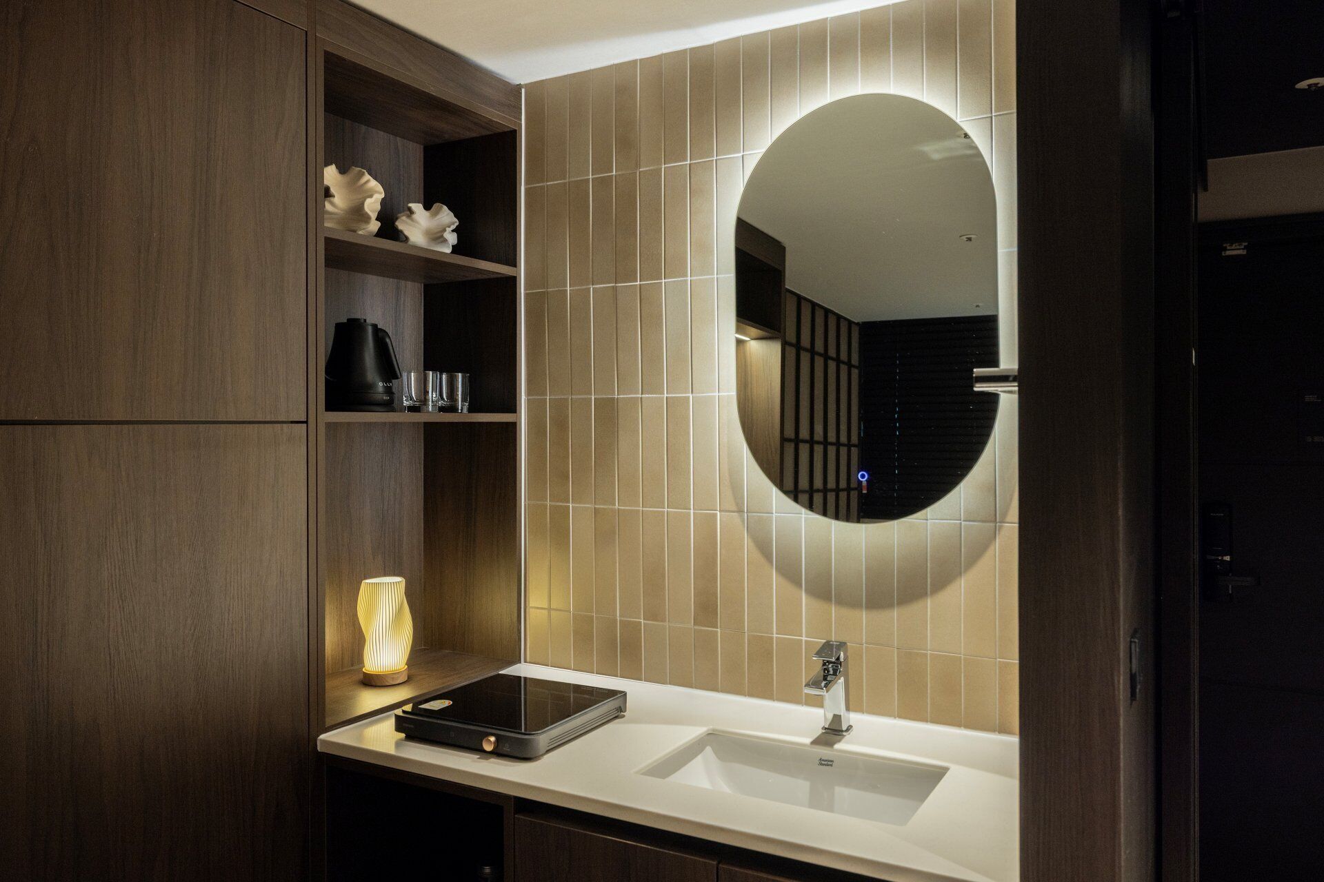 Un baño moderno con un espejo grande, un lavamanos empotrado y una repisa con adornos.