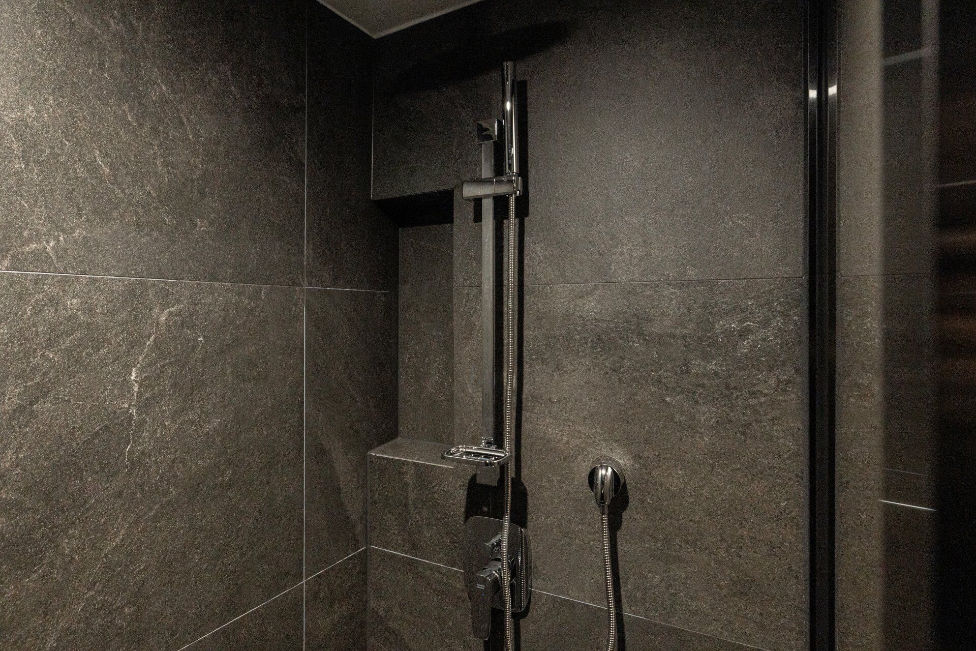 A shower with a handheld showerhead and a wall-mounted faucet.