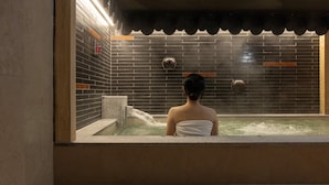 A person sitting in a hot tub with a tiled wall and a clock. - LOOP Seoul Hotel Retreat by Anook Seoul Gangnam 1 (Seoul)