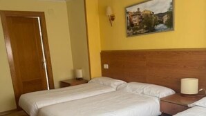 A hotel room with two beds, wooden flooring, a yellow wall, and a painting. - Hostal El Volante (Estella)