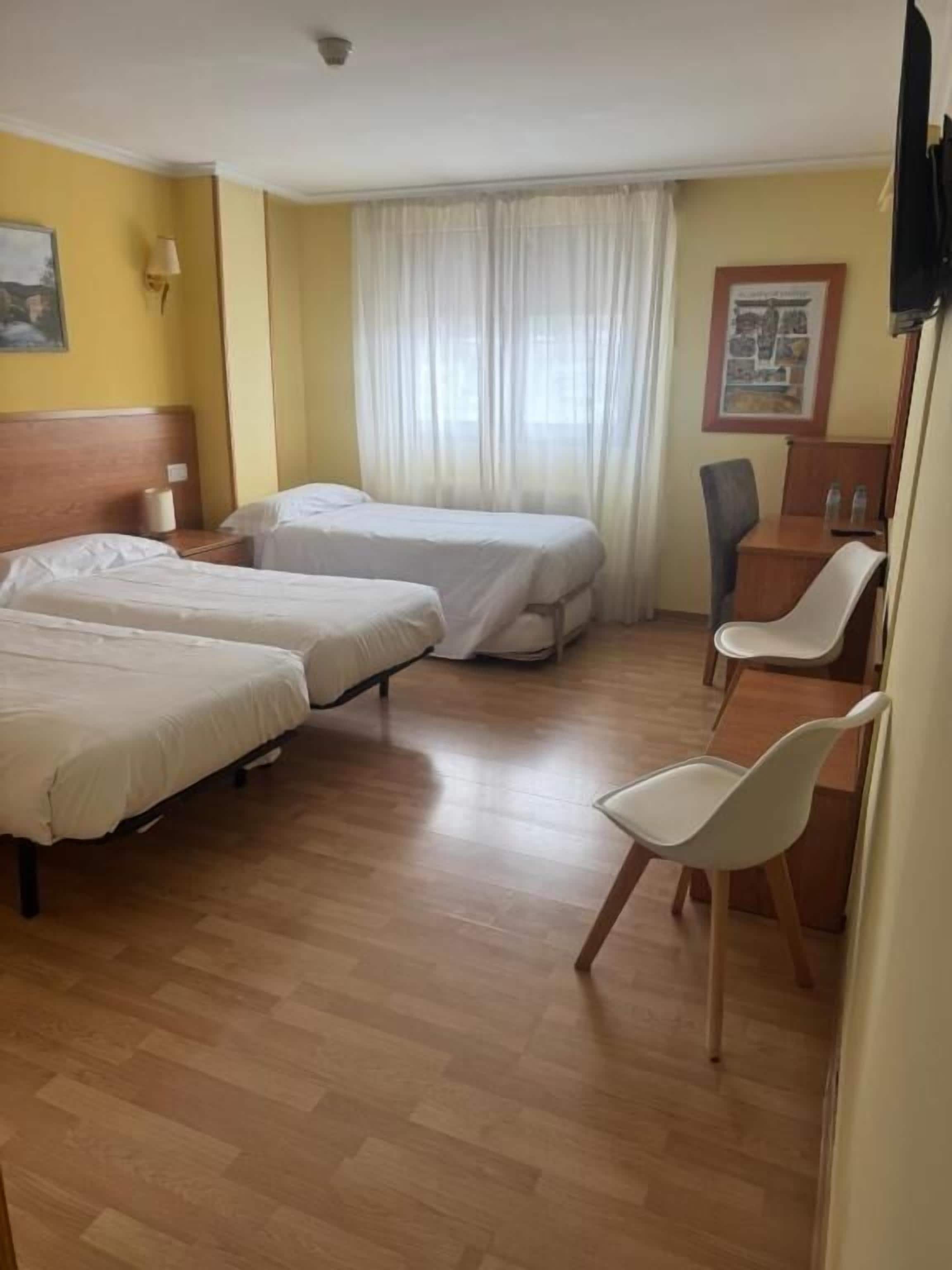 A hotel room with two beds, a desk, a chair, and a window with curtains.