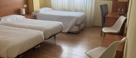A hotel room with two beds, a desk, a chair, and a window with curtains.