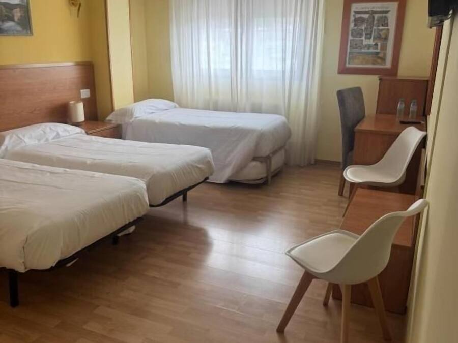 A hotel room with two beds, a desk, a chair, and a window with curtains.